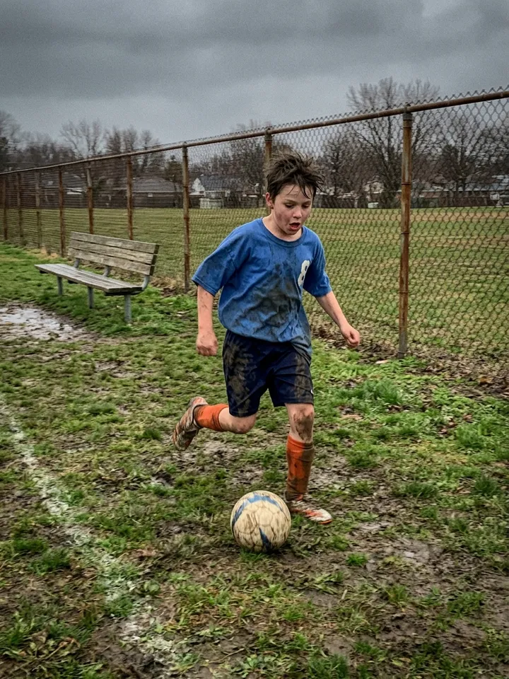 Slide 4: the real photo, a dark-haired boy kicking the ball on a muddy field